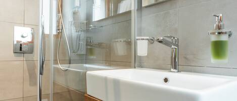 Un baño moderno con cabina de ducha de vidrio, un lavabo blanco y un mueble de tocador de madera.