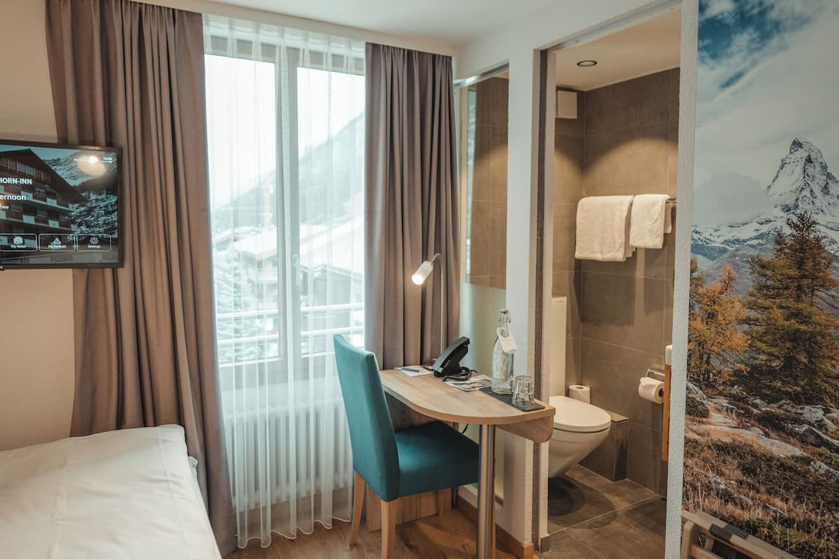 Habitación de hotel con cama, escritorio con silla, televisor montado en la pared y baño con ducha e inodoro.