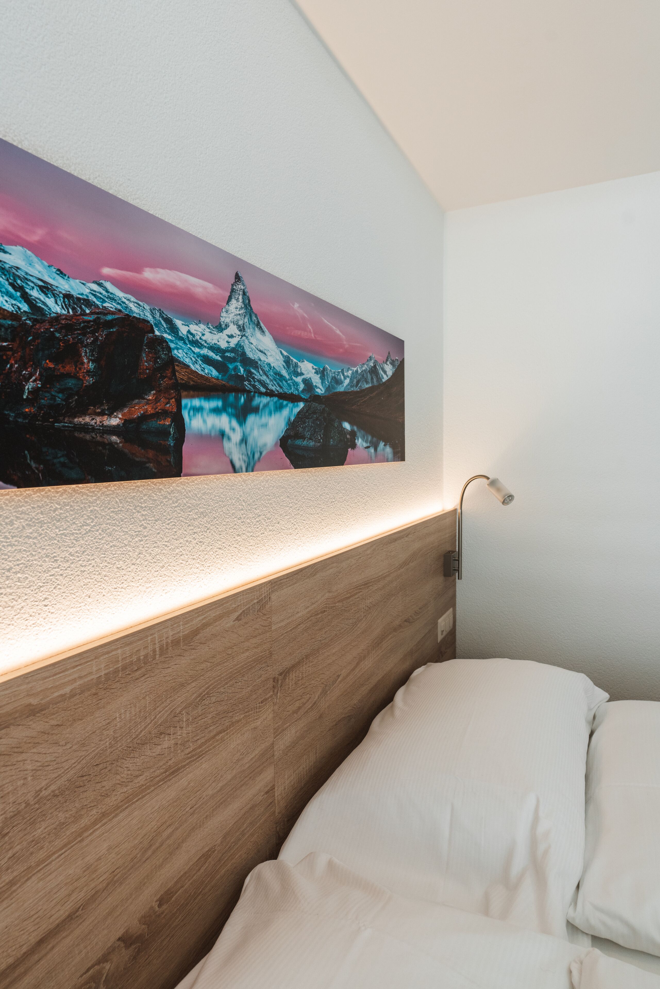 Un dormitorio con cabecera de madera, una lámpara de pared y un cuadro grande enmarcados con un paisaje de montaña.