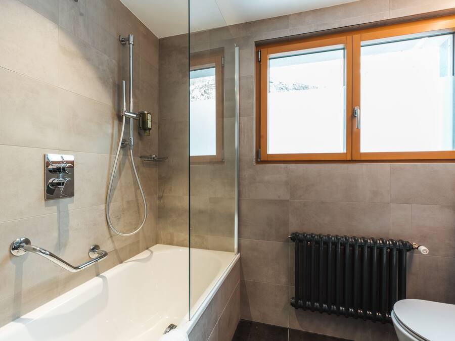 Une salle de bain moderne dotée d’une douche à parois de verre, d’une baignoire, de toilettes et d’une fenêtre donnant sur un paysage enneigé.