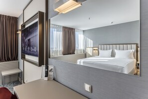 A modern hotel room with a large bed, a desk with a computer, a TV mounted on the wall, and a large mirror reflecting the room. - Hotel Bulgaria Burgas (Burgas)