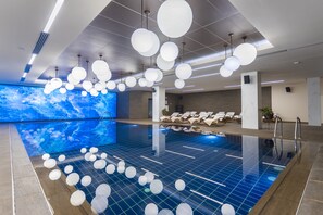 A modern indoor swimming pool with a large digital screen, multiple seating areas, and a ceiling with spherical light fixtures. - Hotel Bulgaria Burgas (Burgas)