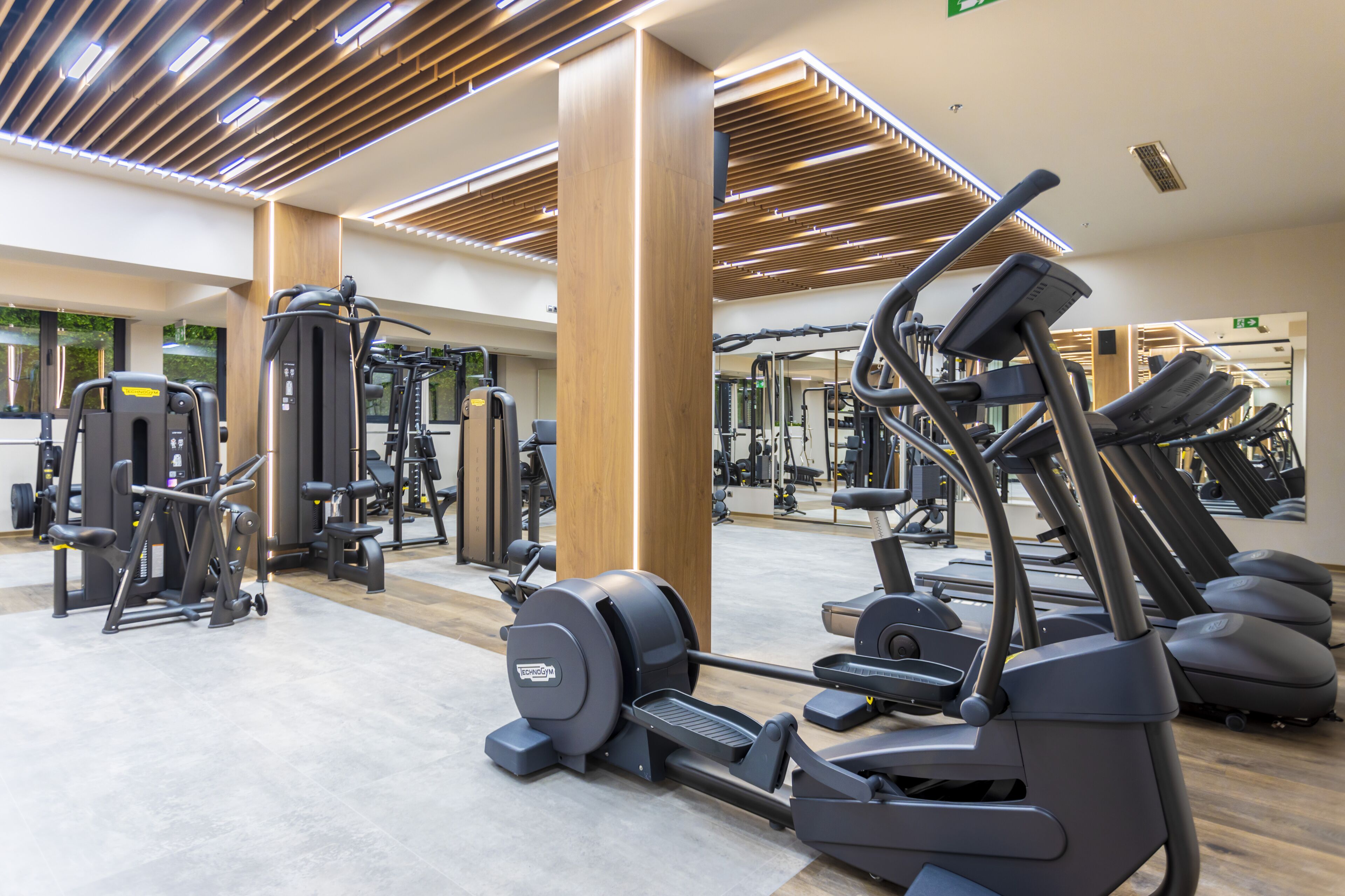 A gym with various exercise equipment, wooden ceiling panels, and a large mirror.