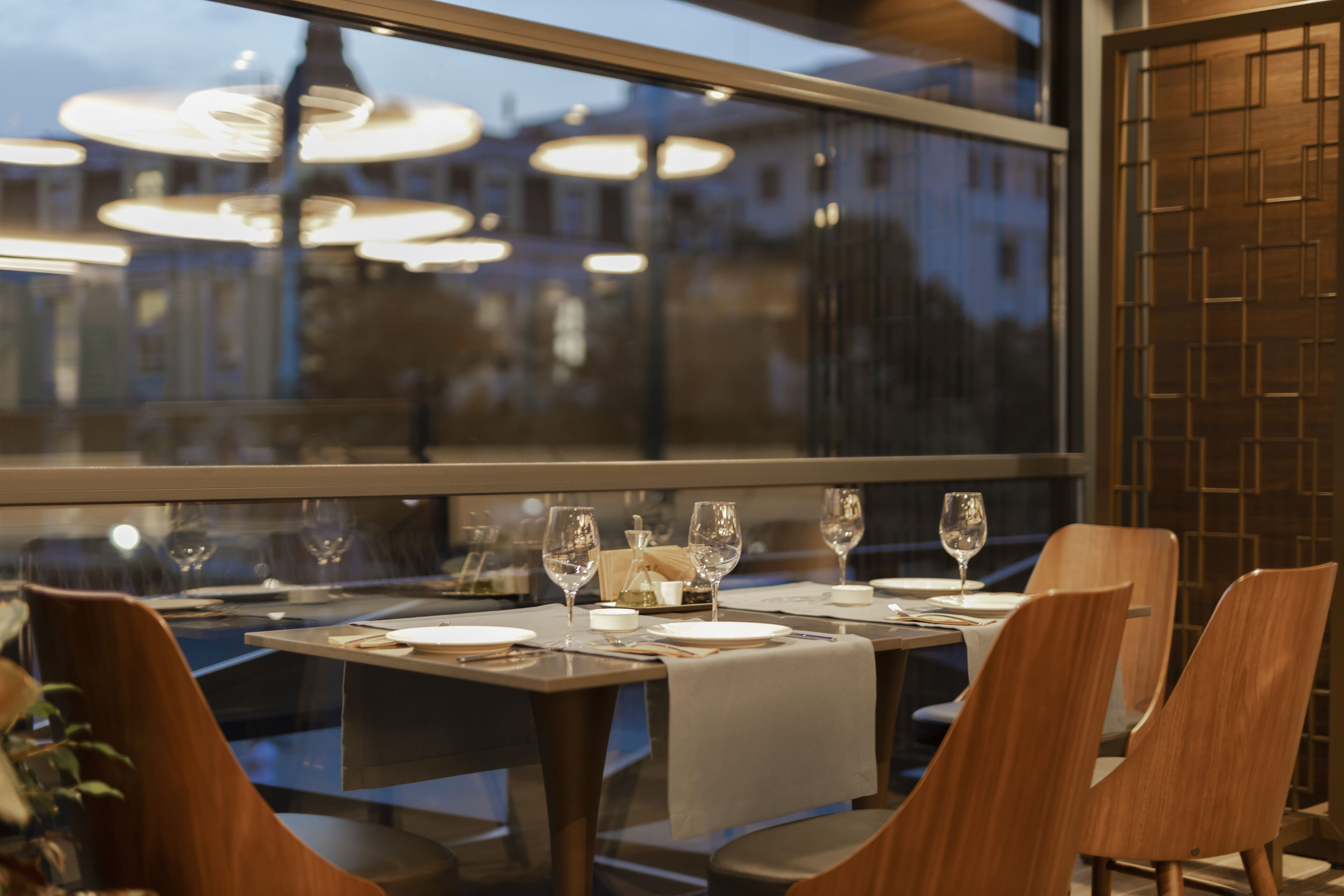 A restaurant with tables set for dining, large windows, and hanging lights.
