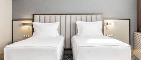 A hotel room with two single beds, each with a headboard and bedside lamps.