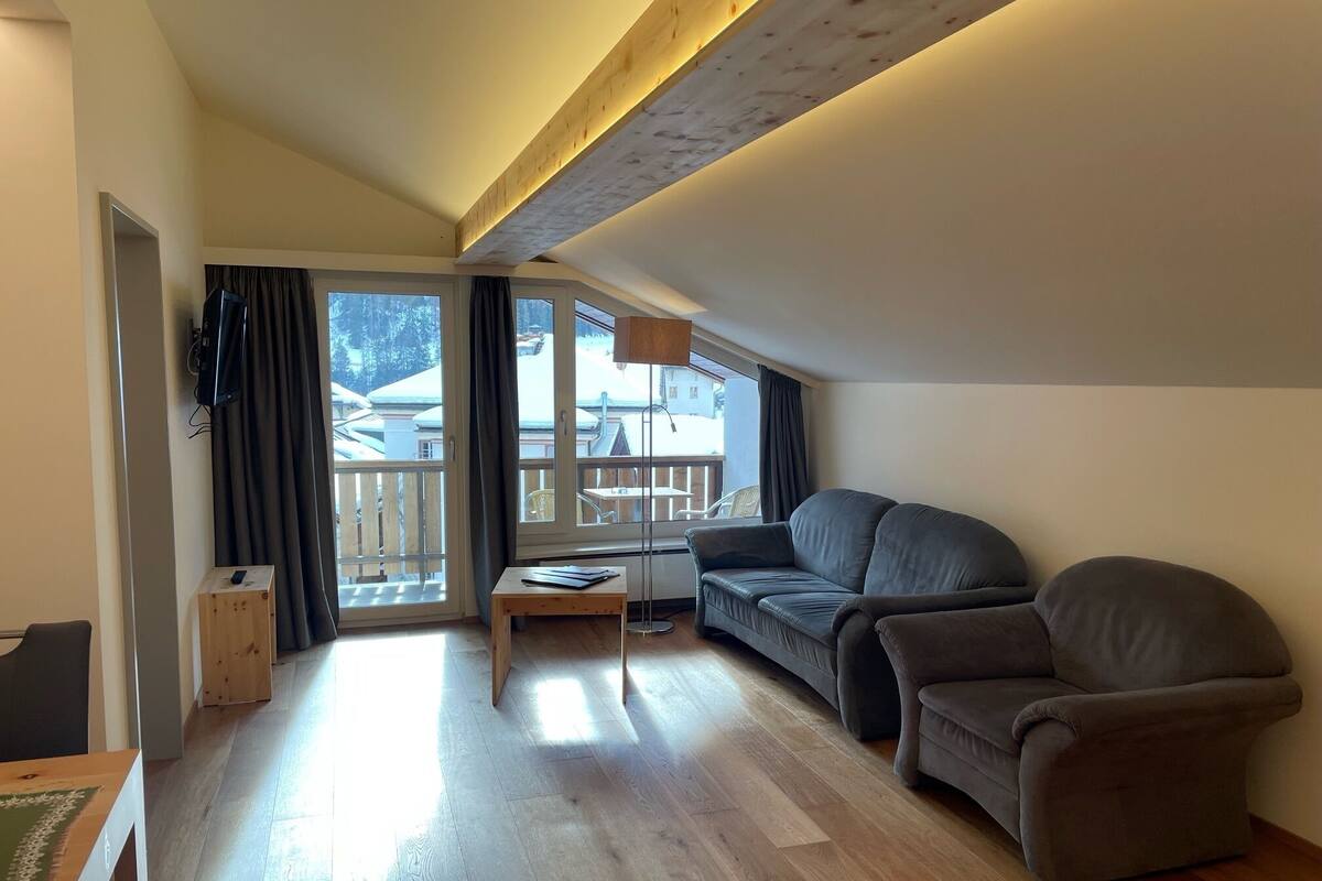 Una sala de estar moderna con sofá, mesa de centro y televisor. Posee un balcón con vistas al exterior.