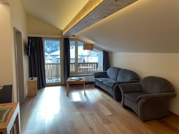 Una sala de estar moderna con sofá, mesa de centro y televisor. Posee un balcón con vistas al exterior.