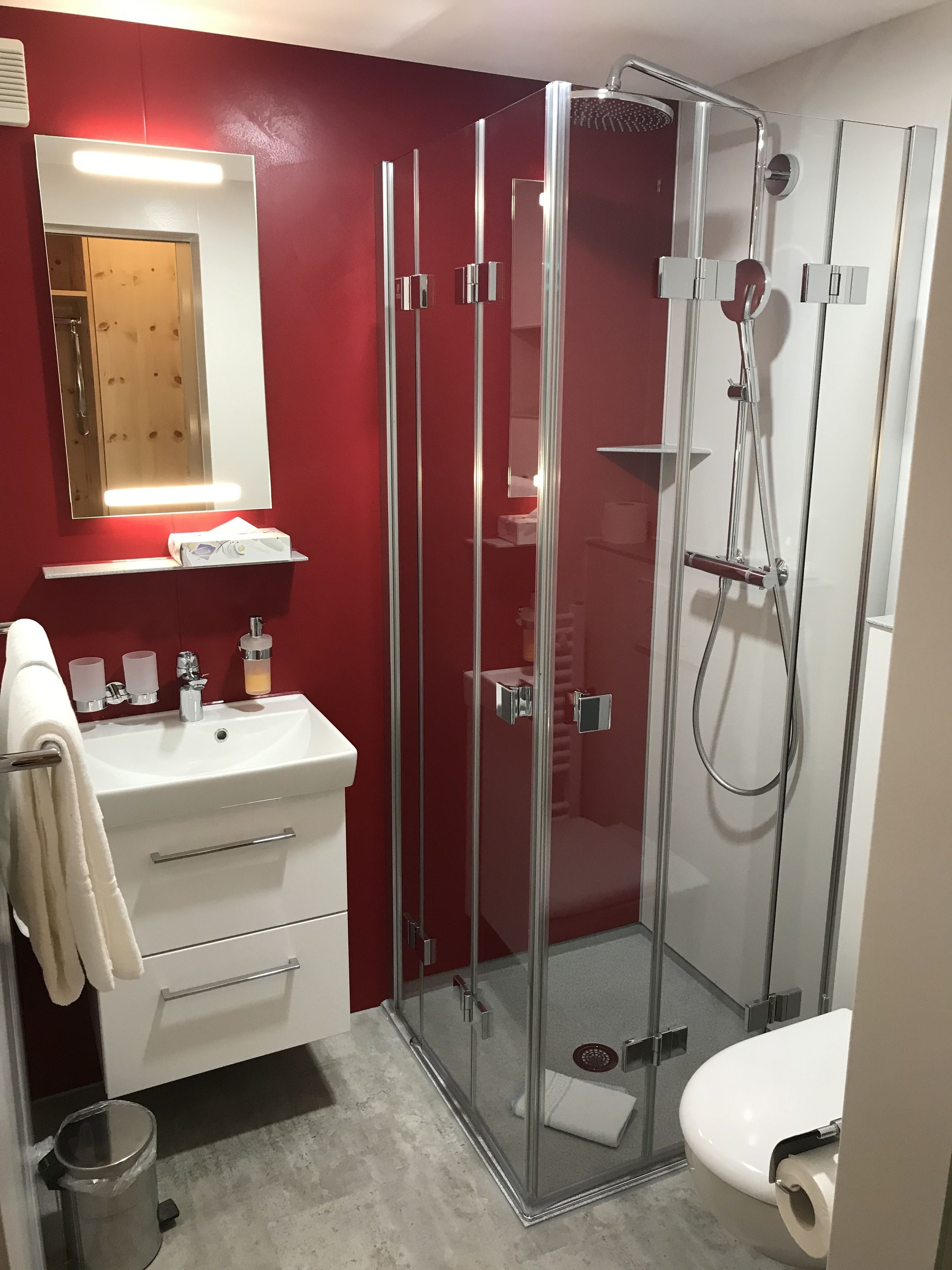 Un baño moderno con ducha de vidrio, un lavamanos blanco con espejo y un inodoro.