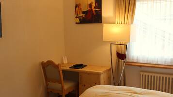 A hotel room with a wooden desk, a chair, a bed, a lamp, and a window with curtains.