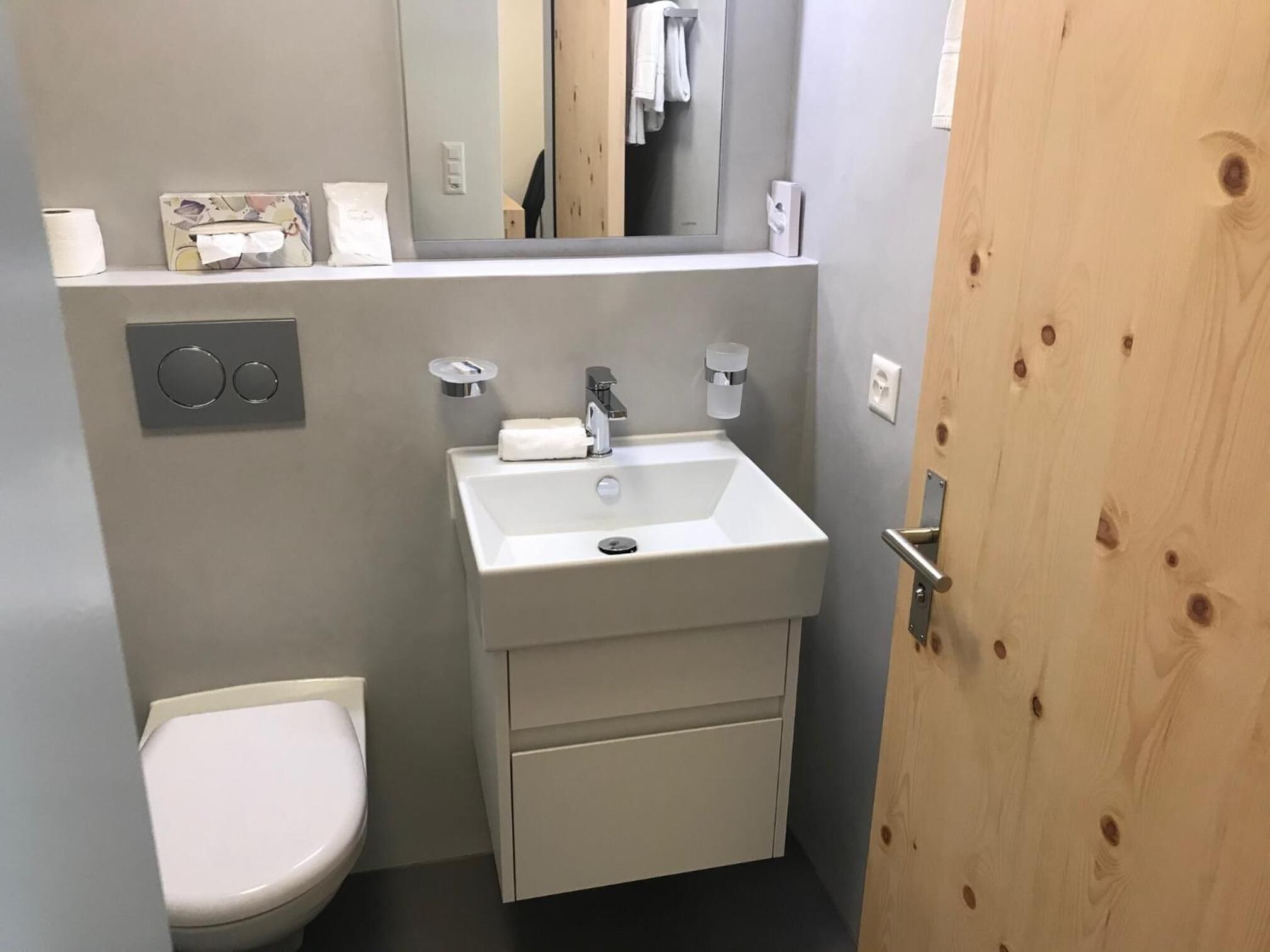 Un baño pequeño y moderno con un lavamanos blanco, un inodoro y un espejo sobre el lavamanos.