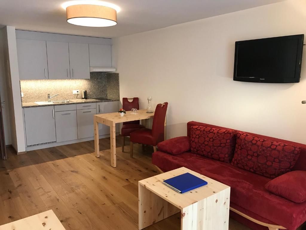 Un espacio habitable compacto con kitchenette, zona de comedor, sofá rojo y televisor de pantalla plana montado en la pared.