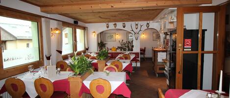 Un restaurante con mesas y sillas de madera, una decoración rojo y blanco, y vistas al exterior.
