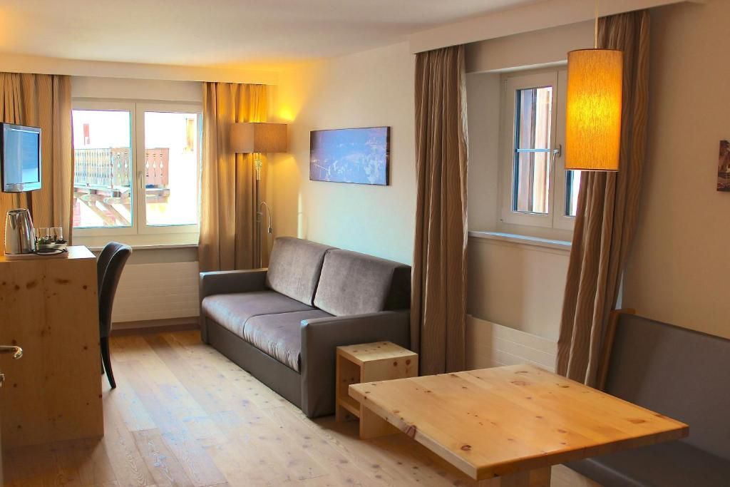 Une chambre d’hôtel avec un canapé, une petite table en bois, une télévision et une fenêtre avec des rideaux.