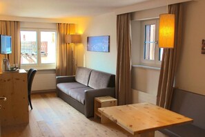 Habitación de hotel con sofá, una mesita de madera, televisor y ventana con cortinas.