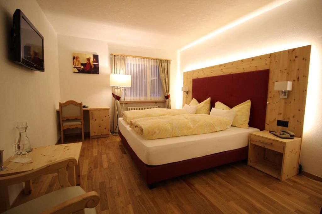 A hotel room with a large bed, bedside tables, a desk, and a television.