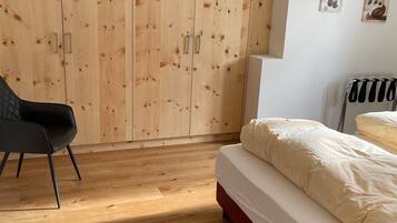 A bedroom with a wooden wardrobe, a bed with white bedding, a black chair, and a radiator.