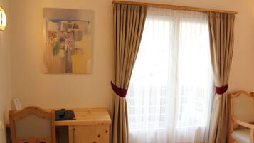 A room with a wooden desk, a chair, a bed, and a window with curtains.