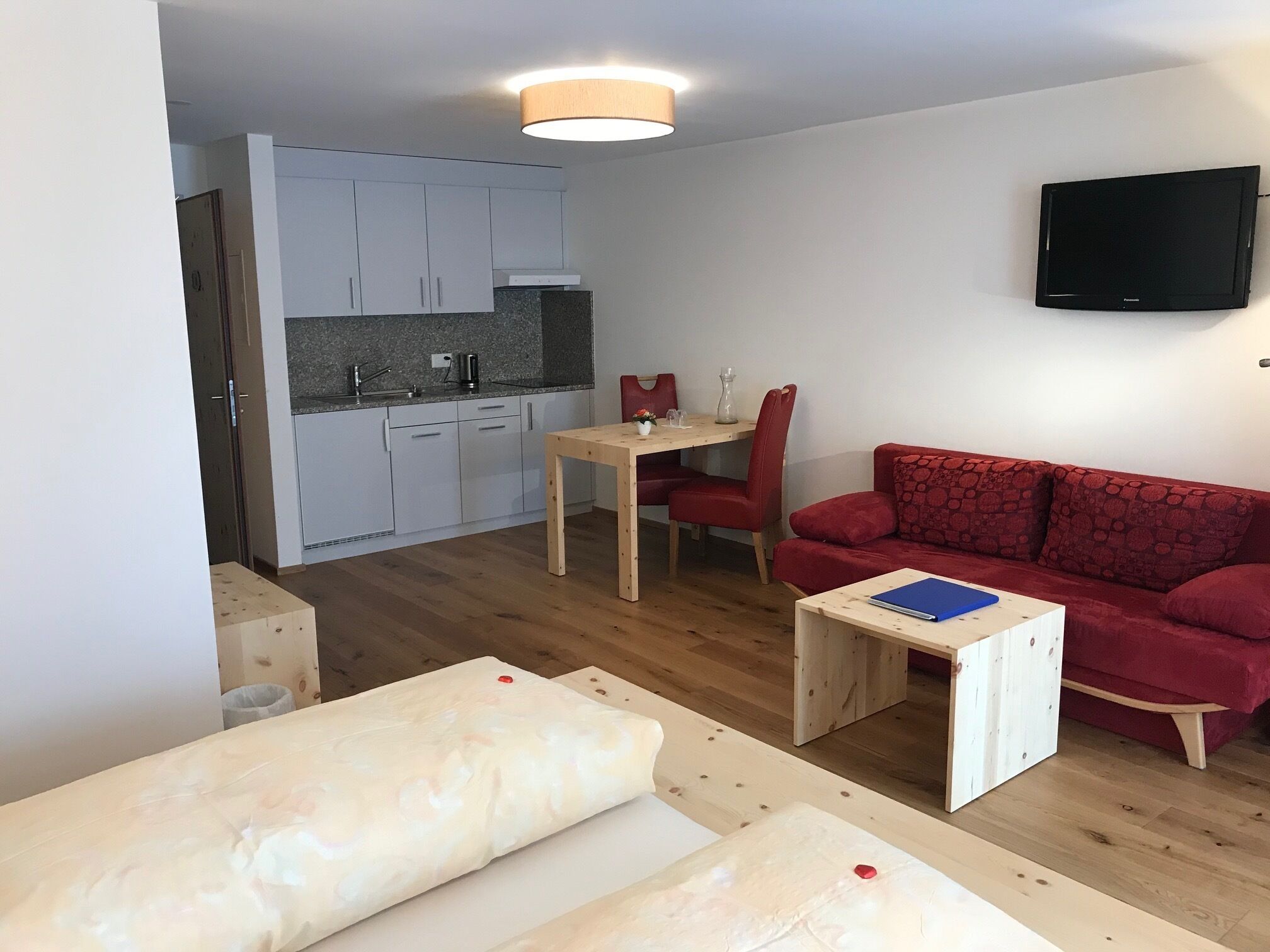 Un espace de vie compact comprenant un coin cuisine, un coin repas, un canapé rouge et un téléviseur fixé au mur.
