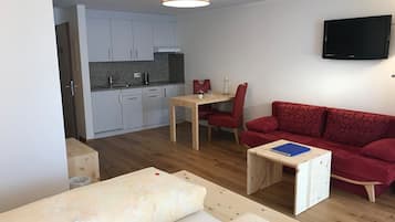 Un espace de vie compact comprenant un coin cuisine, un coin repas, un canapé rouge et un téléviseur fixé au mur.