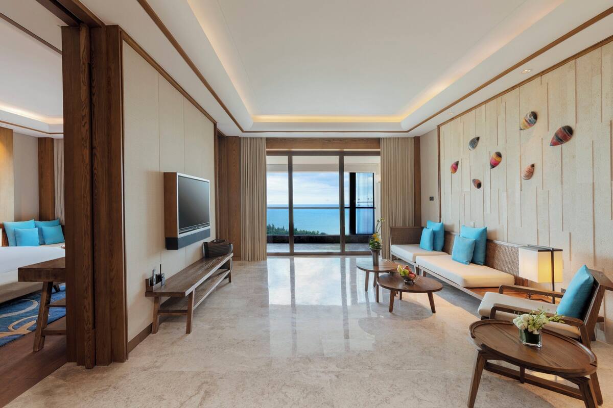 A modern hotel room with a large TV, a sofa, a coffee table, and a view of the sea.