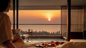 Ein Schlafzimmer mit großem Fenster, einem Bett, einem Nachttisch und Blick auf den Sonnenuntergang.