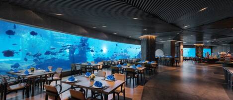 A restaurant with a large aquarium wall, wooden tables, and chairs.