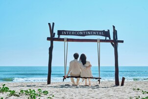 A couple sitting on a swing with a sign that reads 'INTERCONTINENTAL' in front of a beach.