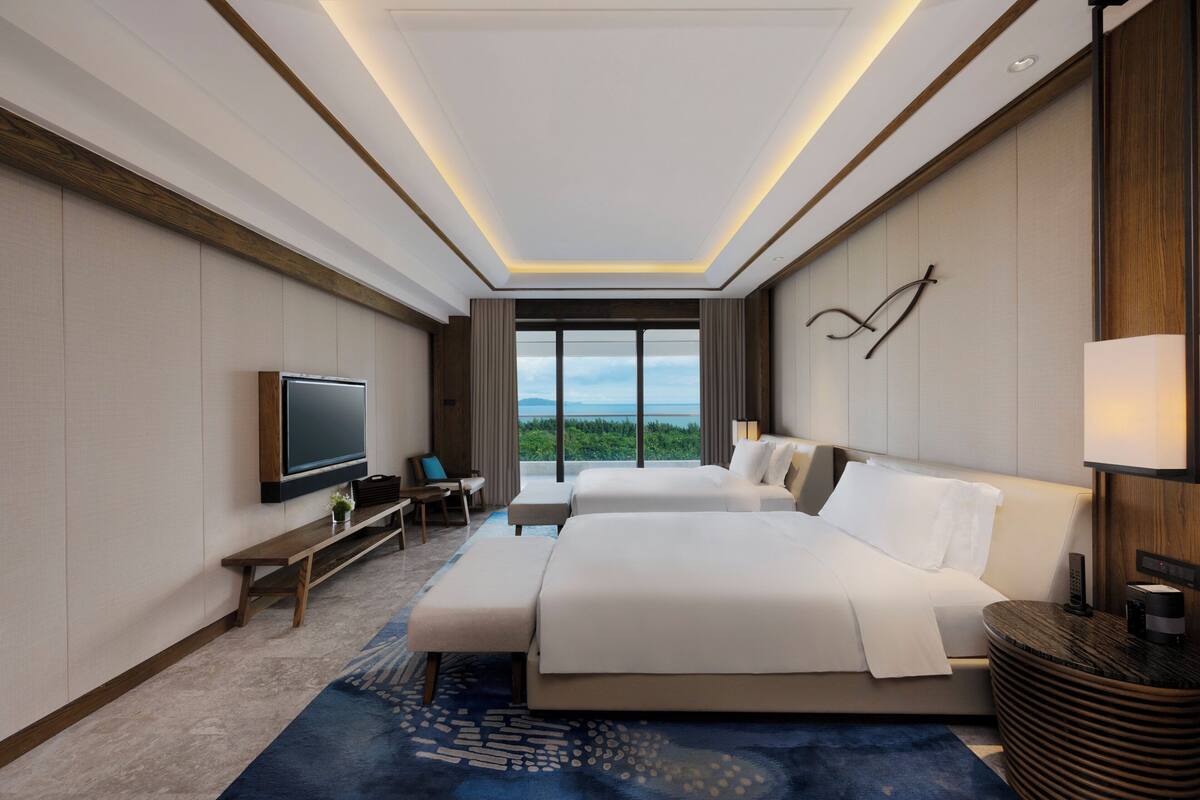 A modern hotel room with a large bed, a television, a desk, and a view of the outdoors.