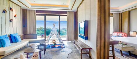 Un'ampia camera d'albergo con una grande finestra, un divano, una televisione e un'area giochi con una tenda teepee e un cavallo a dondolo.