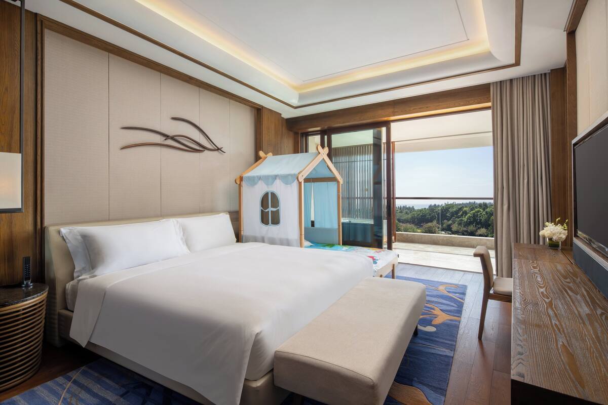 A hotel room with a large bed, a playhouse, a TV, and a view of the outdoors.