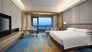 A hotel room with a large bed, a desk, a TV, and a view of the city.