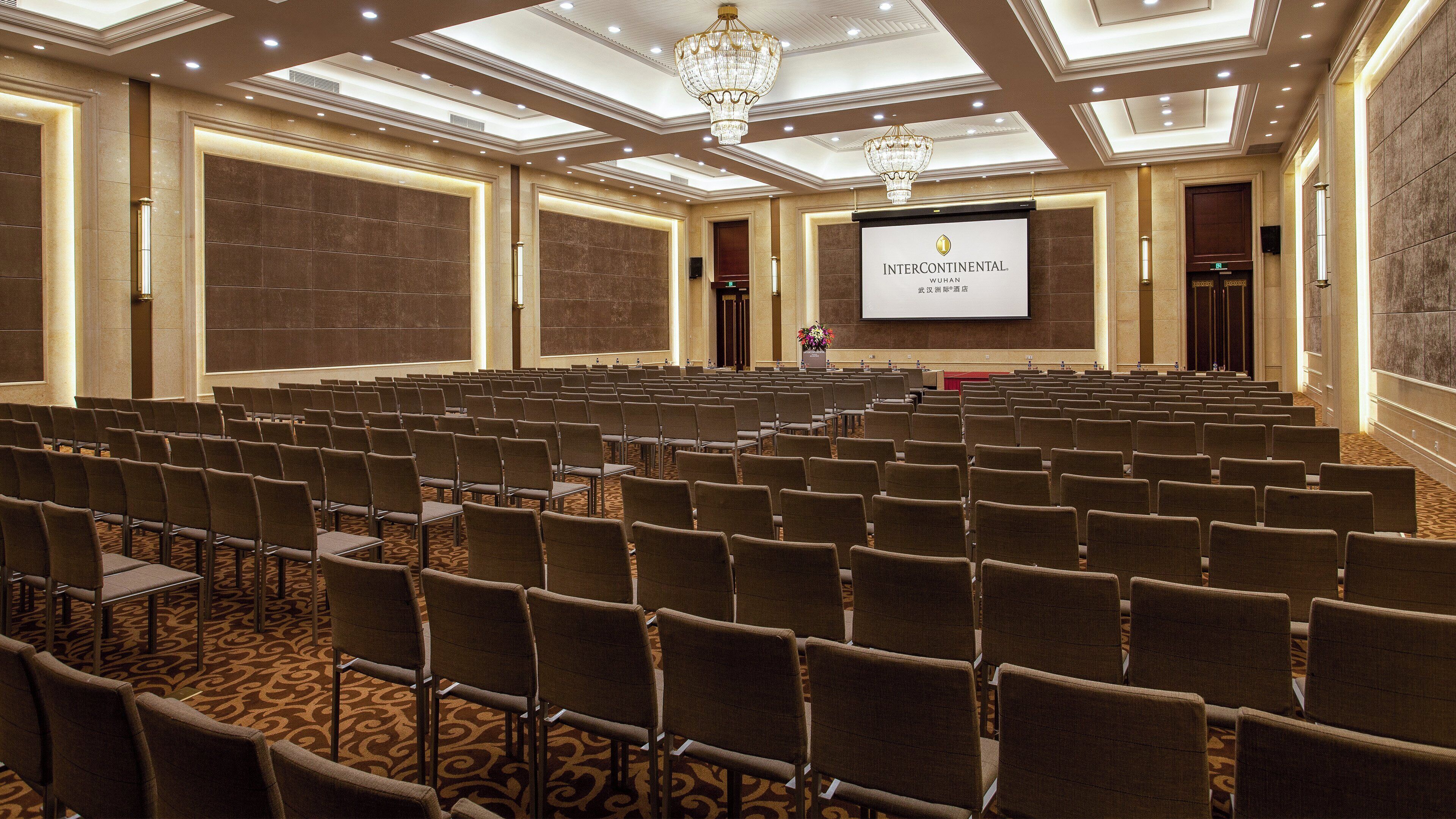 Un salón de conferencias con filas de sillas, una pantalla grande y una araña.