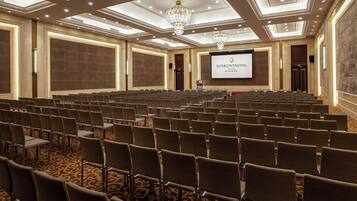 Un salón de conferencias con filas de sillas, una pantalla grande y una araña.