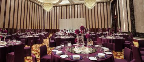 A banquet hall with round tables, purple chairs, and chandeliers.