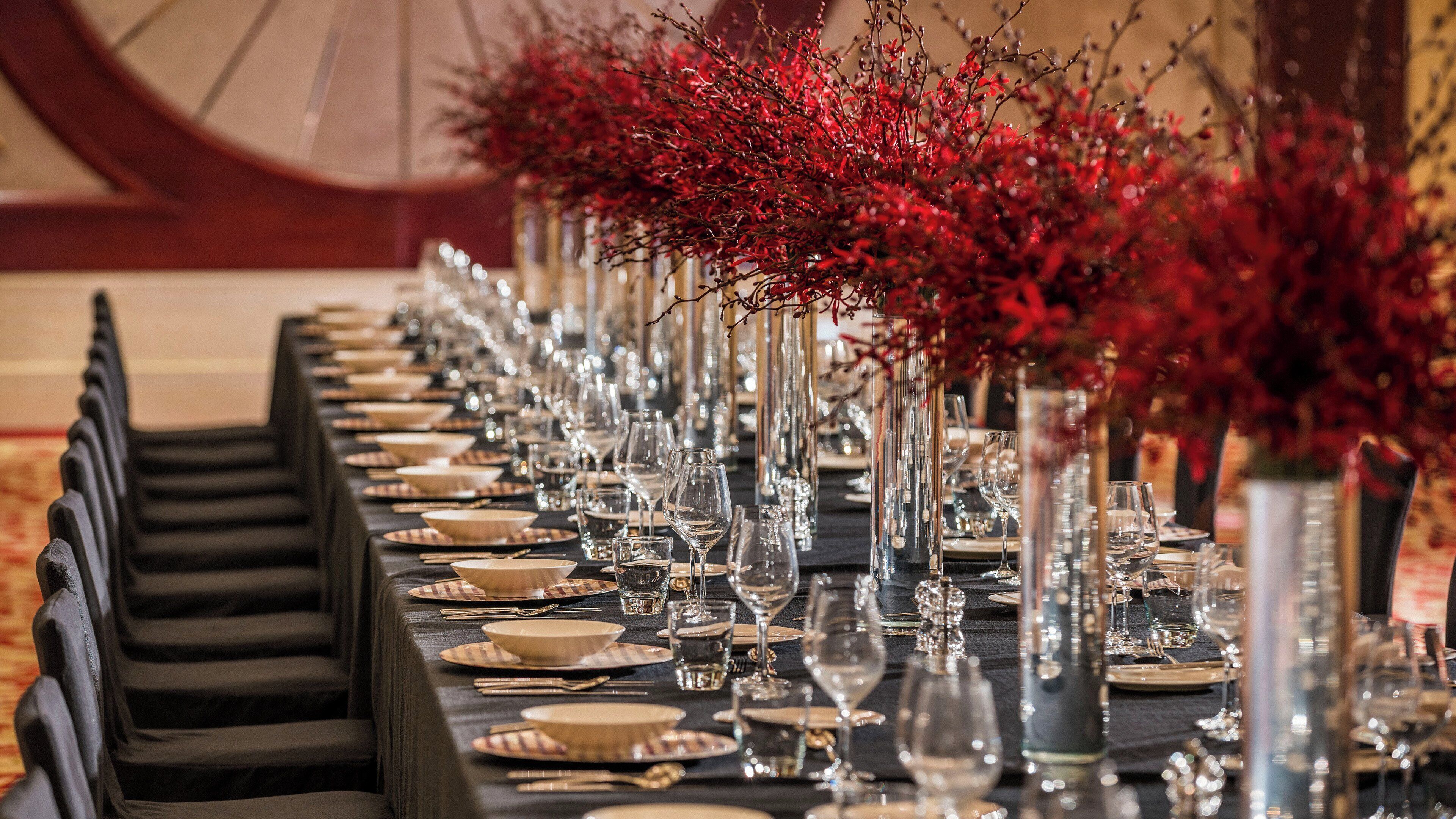 Une longue table à manger, dressée avec de nombreux couverts, comprenant des assiettes, des couverts et des verres à vin.