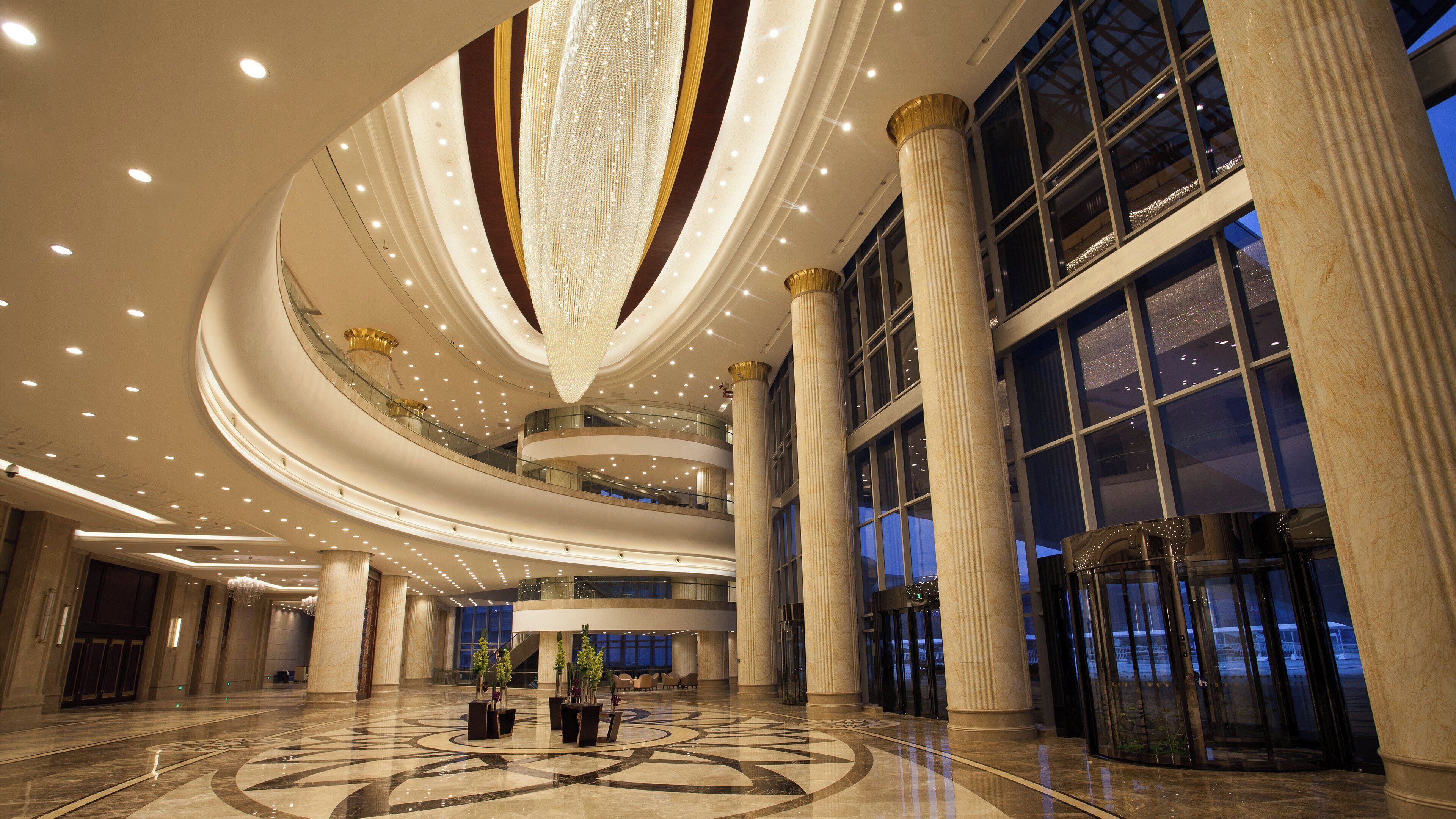 A spacious lobby with a grand chandelier, multiple floors, and large windows.