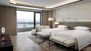 Habitación de hotel con dos camas, un sofá, un escritorio y vistas a la silueta urbana.