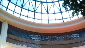 A spacious lobby with a high ceiling and a glass dome, featuring a central display area with various items, seating arrangements, and a polished floor.