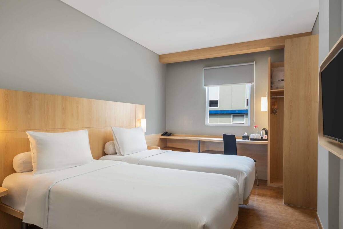 A hotel room with two beds, a desk, a chair, a mirror, and a TV.