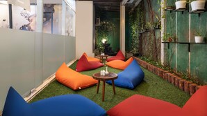 Un área de descanso moderna con cojines de colores, un ventilador de techo y una pared verde con plantas.