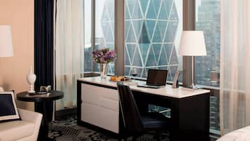 A hotel room with a desk, chair, and a view of a modern building.