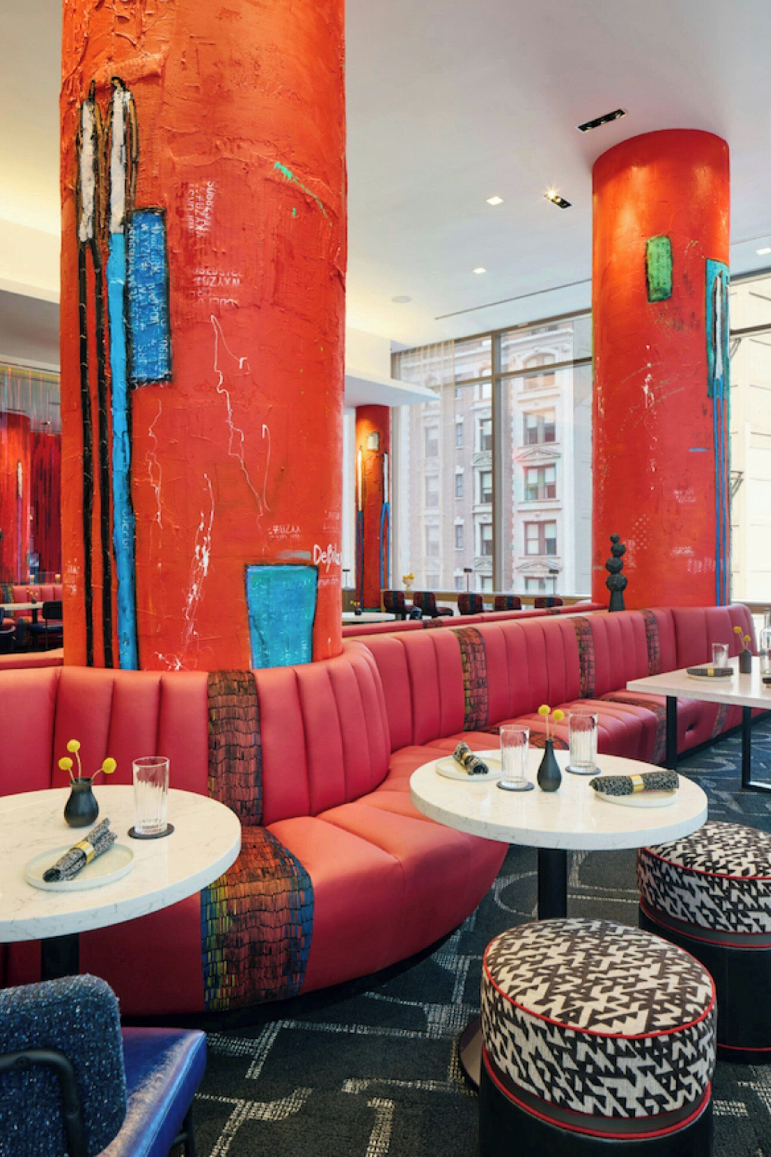 A modern interior with a curved red seating area, round tables, and patterned ottomans.