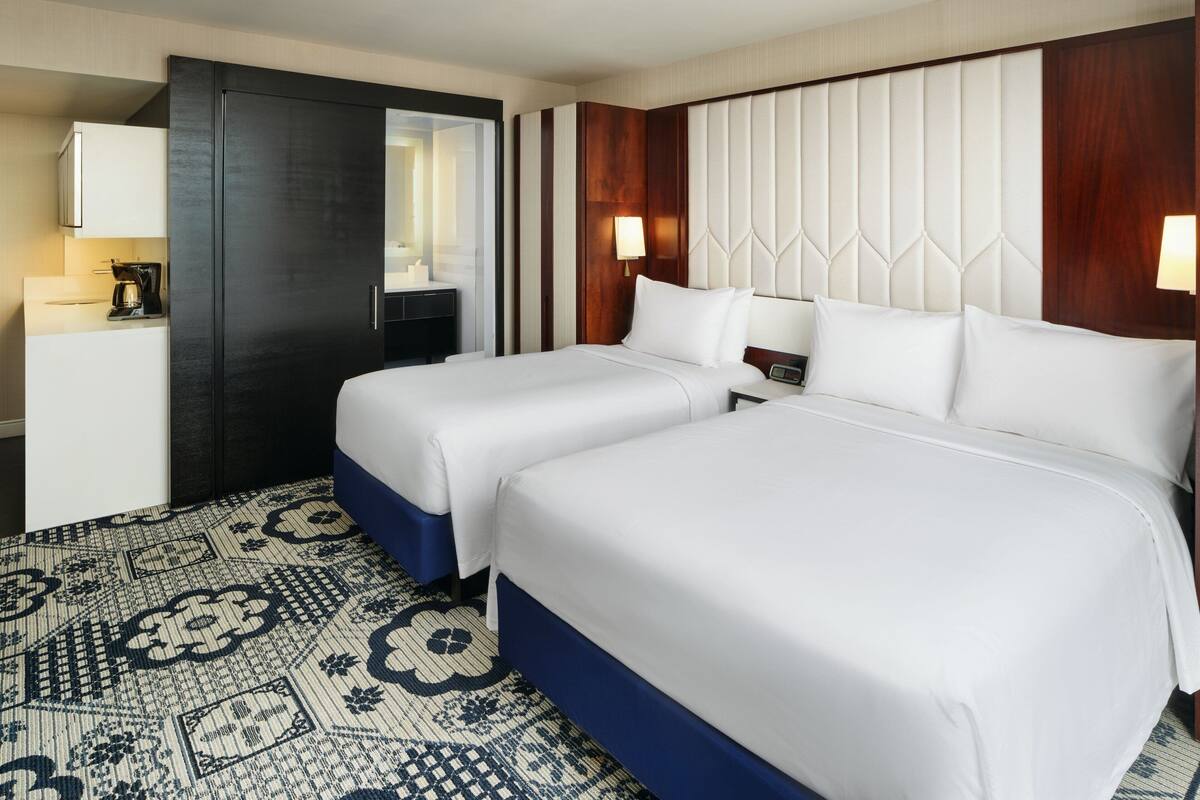 A hotel room with two beds, a desk with a coffee maker, a mirror, and a patterned floor.