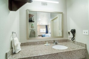 A bathroom with a granite countertop, a white sink, a large mirror, a towel rack, and a hairdryer on the wall.
