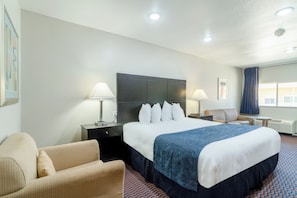 A hotel room with a large bed, two bedside tables with lamps, a sofa, and a small table.