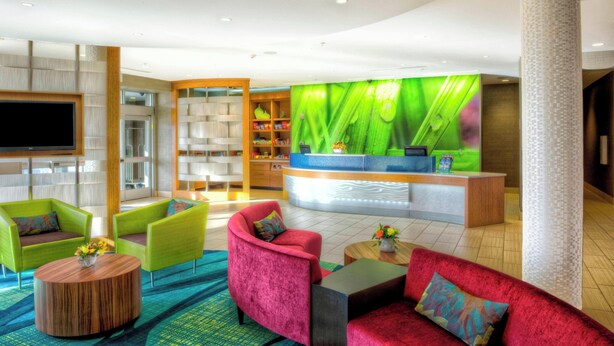 A modern lobby with vibrant green and red seating, a reception desk, and a large green wall with a leaf design. - Springhill Suites by Marriott Bellingham (Bellingham)