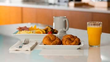 A breakfast setting with croissants, orange juice, and a coffee mug on a table.