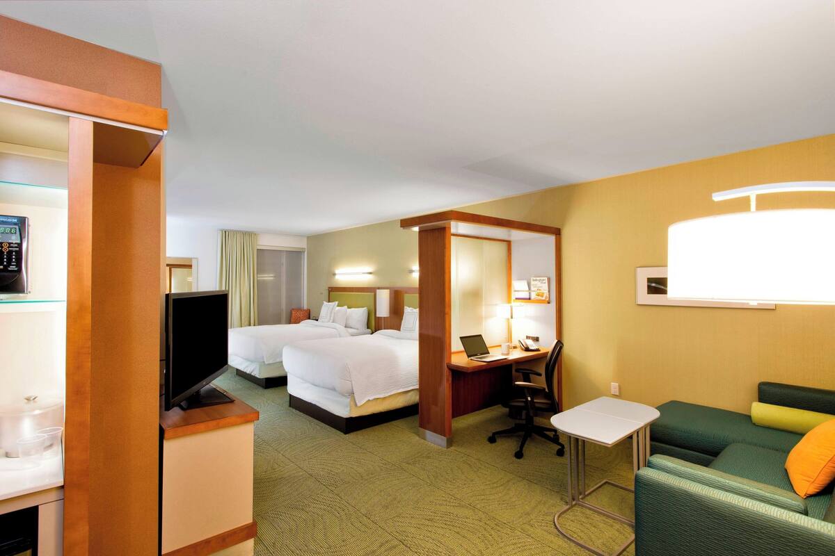 A hotel room with two beds, a desk with a laptop, a television, and a sofa.