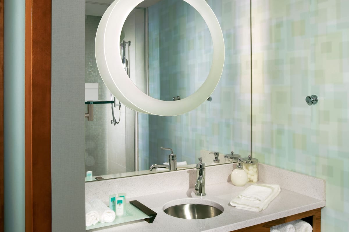 A bathroom with a wooden vanity, a round mirror, a sink, and a towel rack.