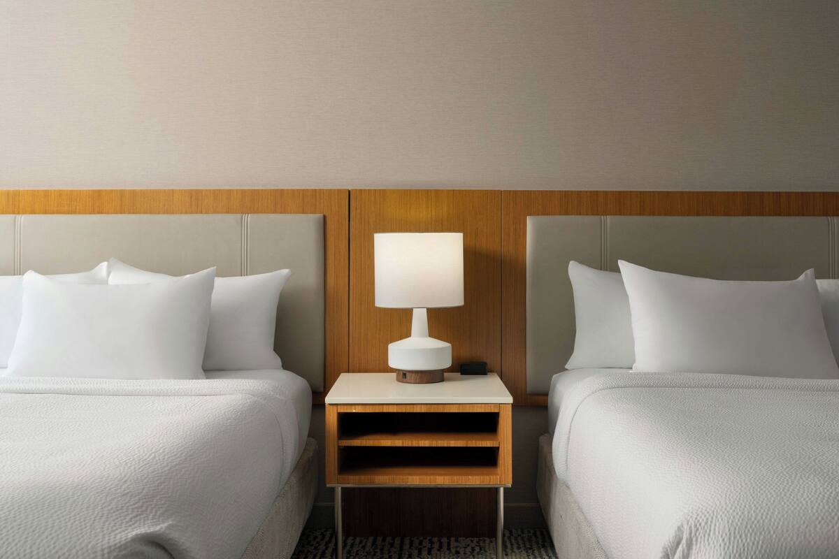 Une chambre d’hôtel avec deux lits, une table de chevet avec une lampe et une tête de lit en bois.